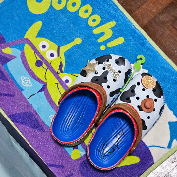 Pair of Pixar Toy Story Woody themed Crocs clogs with charms placed on cute Alien character mat on August 28, 2024 in Bangkok,  Thailand 
