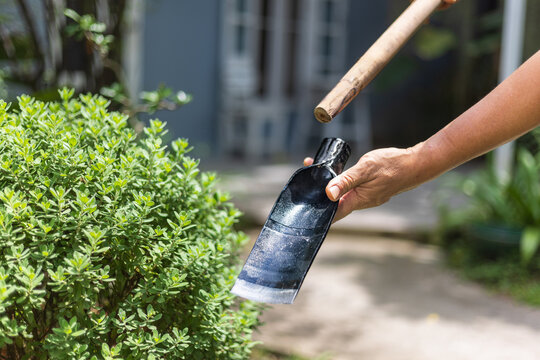 An senior man repairing and attaching a wooden handle to a narrow spade blade in a backyard garden.