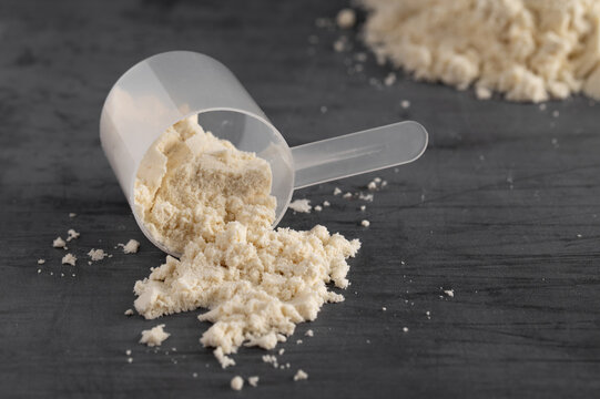 Measuring scoop with protein powder spilled on a dark background