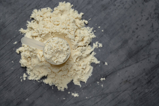 Scoop resting on a pile of protein powder on a dark background