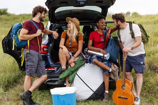 Friends Loading Camping Gear Into Car at Outdoor Location on Sunny Day