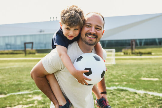 man with child playing football outside on field
