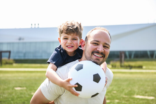 man with child playing football outside on field