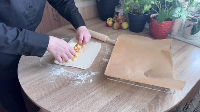 Rolling puff pastry around apple filling to shape homemade apple strudel