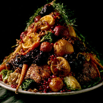 Festive roast meat platter with vegetables garnished with fresh herbs and berries