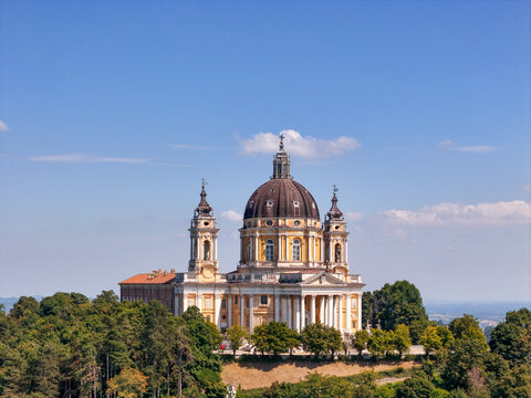 Aerial view of the Basilica of Superga, a historic baroque church with a prominent dome and bell towers, surrounded by lush green trees in Turin, Piedmont, Italy.