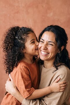 Happy loving Hispanic mother hugging her cute little daughter with curly hair while sharing a joyful warm moment together