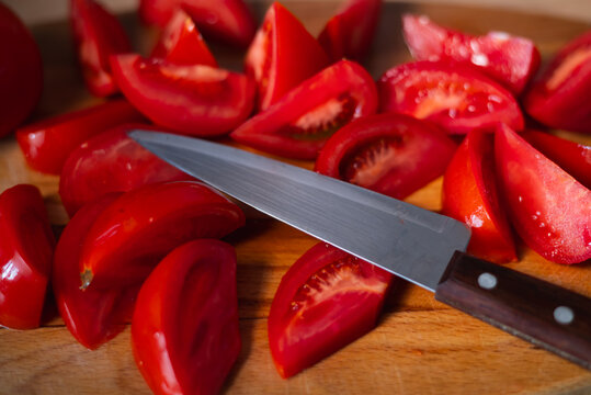 Tomatoes are cut into wedges and arranged on a wooden cutting board. A knife lies next to the raw ingredients, suggesting a meal preparation activity