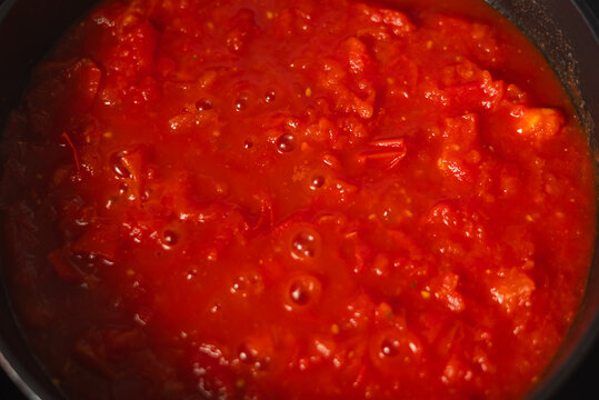 A pot of tomato sauce simmers on the stove, with bubbles forming on the surface. Bright red tomatoes blend with spices, creating a rich aroma in the kitchen