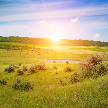Scenic morning landscape with sun rising above rolling meadows grassy slopes and small pond at dawn