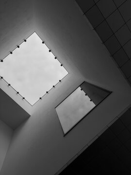 Square skylight and wall mirror create diagonal lines and layered reflections in a monochrome interior.