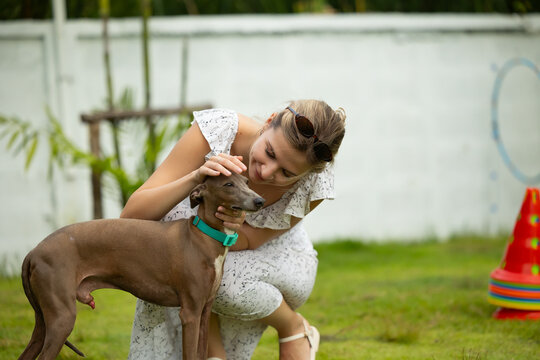 young caucasian woman embraces her gray Italian Greyhound dog, appearing relaxed and content. Home pets. woman holding and hugging her cute dog while walking in the park Outdoor