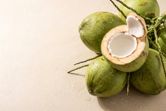 Fresh young green coconuts with opened coconut on cream stone background and copy space