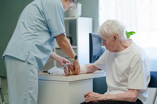 Nurse bandaging elderly man with broken arm and cast in hospital. Healthcare professional applying wound care and dressing to injured senior patient with gentle trust and reliable support indoors