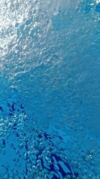 Close-up overhead footage of bubbles and turbulent water created by a swimming pool return jet, forming a dynamic pattern on the water surface.