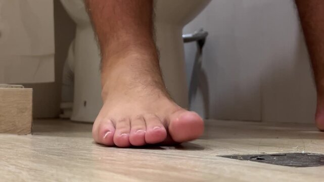 Horizontal video close up. Bare male hairy legs without pedicure. White naked man sits on toilet in hotel bath room, public WC, apartment, hostel restroom. Concept of clean, diarrhea, intestines, inn