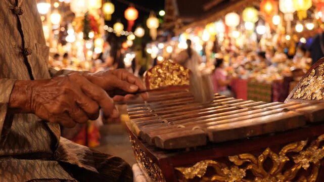 Elderly Thai man plays traditional xylophone instrument at night market