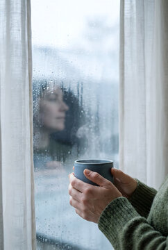 Manos sosteniendo una taza de caf&eacute; caliente junto a una ventana con gotas de lluvia en un d&iacute;a fr&iacute;o y acogedor