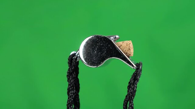Silver metallic basketball whistle swinging gently on a black lanyard against a green screen backdrop