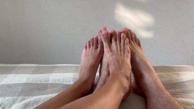 Close-up of a couple's bare feet resting and wiggling on a sunlit bed in the morning. Relaxed lazy atmosphere in a bedroom.