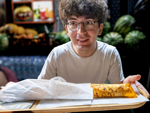 Istanbul, turkey. August 2, 2025. Young man holding a tray with two traditional turkish durum wraps, ready to eat street food in istanbul, turkey