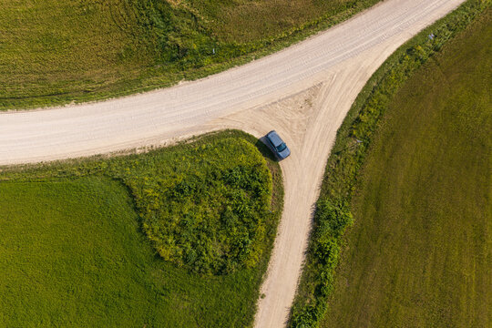 Aerial view of a car parked at a fork in a gravel road surrounded by green fields in Juzintai, Panevezys County, Lithuania.