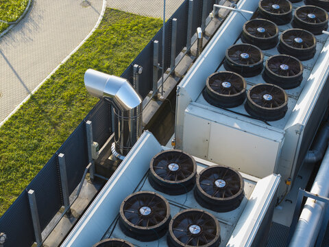 Aerial view of industrial HVAC cooling units on a rooftop with metallic ventilation pipes and green grass area in the background in Krakow, Lesser Poland Voivode, Poland.