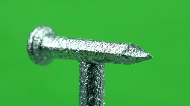 Galvanized steel masonry nail rotating slowly on a bright green chroma key background for construction isolation