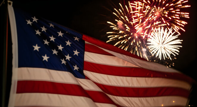 American flag waving with Fourth of July fireworks display. Patriotic USA celebration featuring red, white, and blue explosions in night sky.