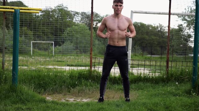 Male shirtless athlete doing squats at sports ground. Young sportsman working at summer nature. Strong sporty man exercising outdoor. Concept of active and sportive lifestyle. Slow motion