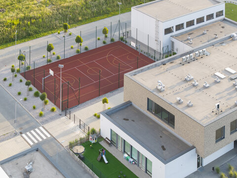 Aerial view of a modern school building with a red basketball court and a small playground in Krakow, Lesser Poland Voivode, Poland.