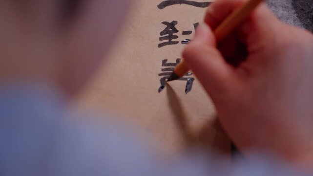 Holding a small brush and writing word by word on brown paper