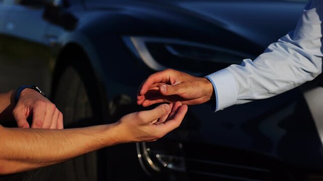 Male hand giving key of car to buyer of electric automobile outdoor. Handshake between salesman and new owner of modern auto after successful deal. Concept of buy or rent car. Slow mo
