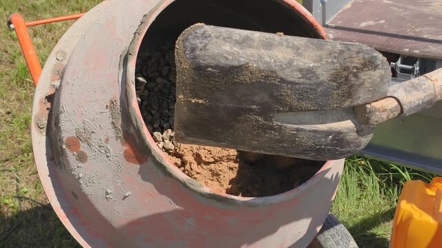 Batch preparation involves shoveling sand and gravel into cement mixer at construction site. Batch preparation ensures proper material ratio, creating strong concrete mixture for building projects.