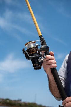 Low angle view of fisherman holding fishing rod with spinning reel against blue sky