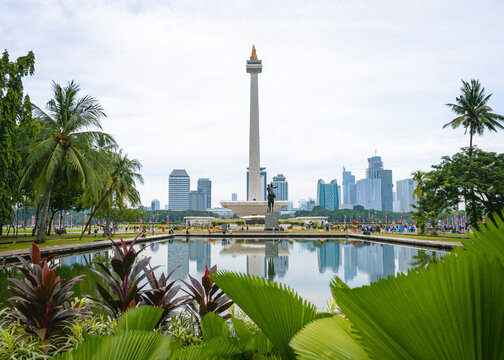 Jakarta, Indonesia - August 5, 2026: National Monument (Monas) reflected in a pond with the Jakarta skyline in the background, surrounded by tropical gardens under daylight.