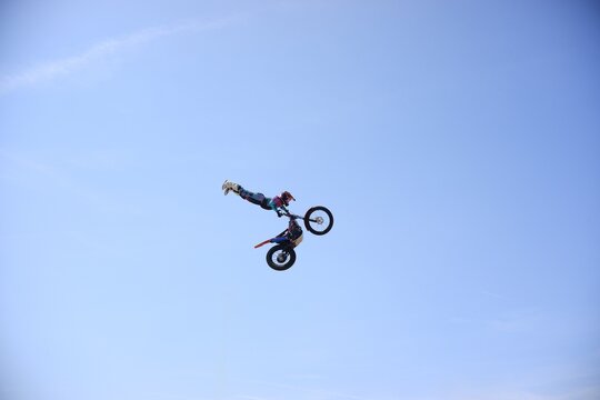 Freestyle motocross rider performing extreme aerial stunt jump against clear blue sky with copy space
