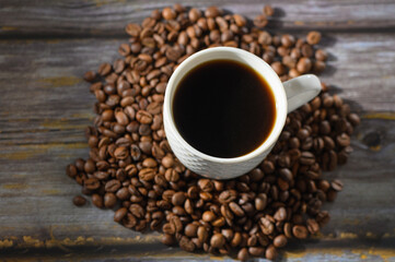 Fototapeta premium Top view of coffee cup surrounded by roasted coffee beans on wooden background