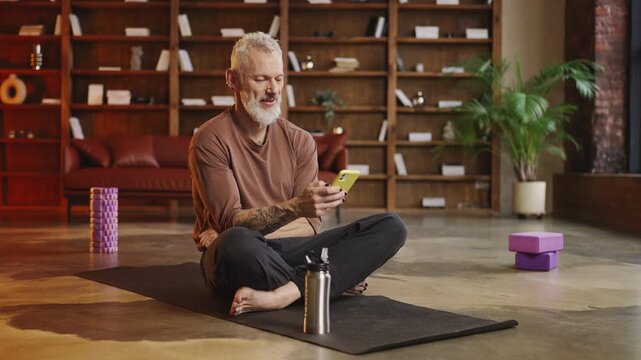 Tattooed man in his 50s browsing a fitness app and choosing a yoga exercise