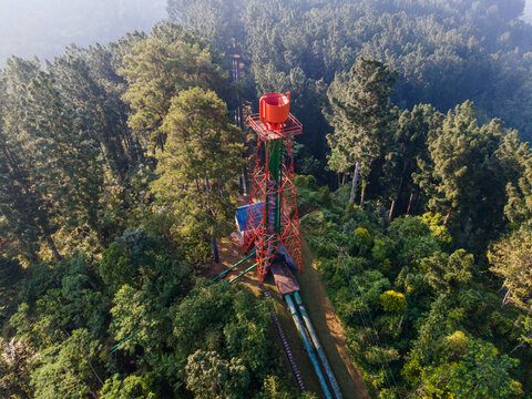 Aerial view of the Ketenger hydroelectric power plant surge tank and penstock structure surrounded by dense tropical forest in Baturaden, Central Java, Indonesia.