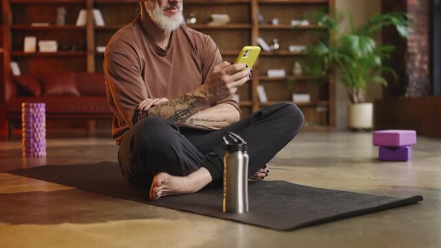 Smiling tattooed man in his 50s using a fitness tracker app after a workout