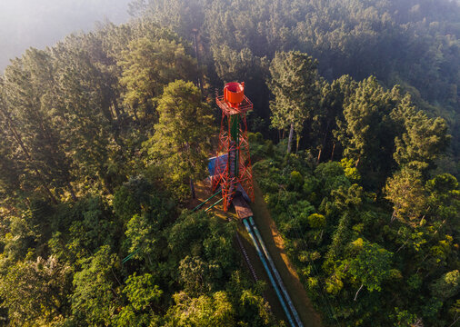 Aerial view of the Ketenger power plant structure surrounded by dense pine forest and lush greenery in Baturaden, Central Java, Indonesia.
