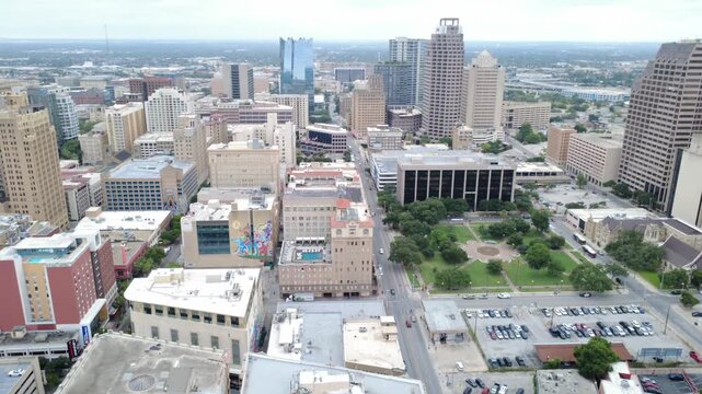 Downtown civic center lush green lawns of Travis Park border commercial office buildings, historic structures in downtown San Antonio. Street grids connect municipal zones, skylines background, TX