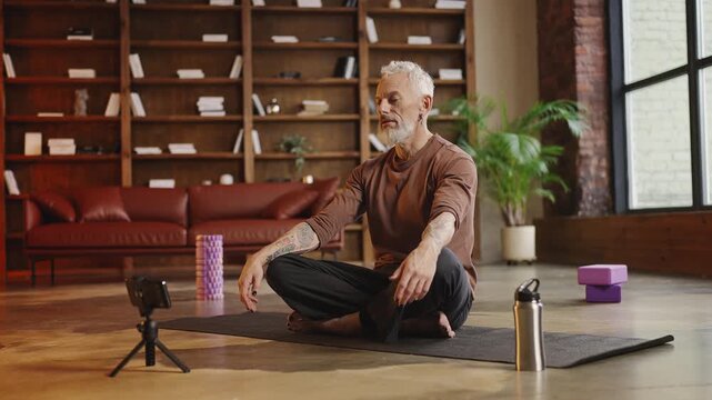 Toned tattooed man recording a yoga tutorial while performing an asana