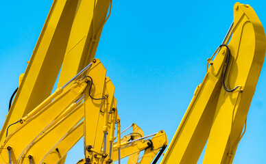 Closeup yellow hydraulic excavator arm with piston cylinder against blue sky, heavy construction machinery, industrial engineering equipment and mechanical technology background. Mechanical industry. © Fahroni