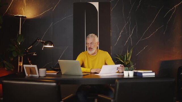 Stylish businessman in his 50s having a work video call on a laptop in office