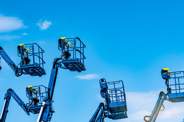 Articulated boom lift fleet with telescopic aerial work platforms against sky. Construction equipment rental, industrial maintenance, hydraulic access systems, engineering services and elevated work. © Fahroni
