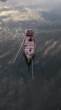 Two people in a wooden boat rowing on a calm lake with reflections of clouds in the water serene