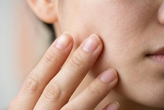Close up of natural skin texture on woman face, showing detailed skin texture for dermatology analysis while hand touching authentic skin texture for skincare beauty treatment.