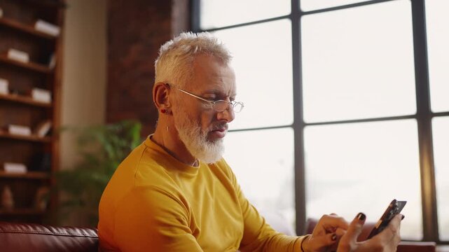 Smiling man in his 50s texting while resting on a sofa, mobile dating app